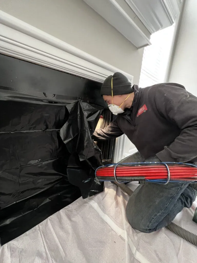 Barnhill Chimney technician performing a chimney sweep inside a Lexington home with drop cloth and equipment